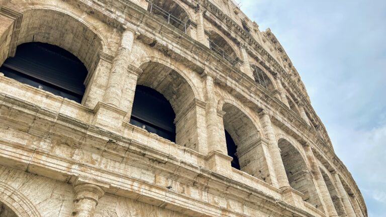 This image shows an upward view of the iconic Roman Colosseum, showcasing its grand arches and ancient travertine stone...
