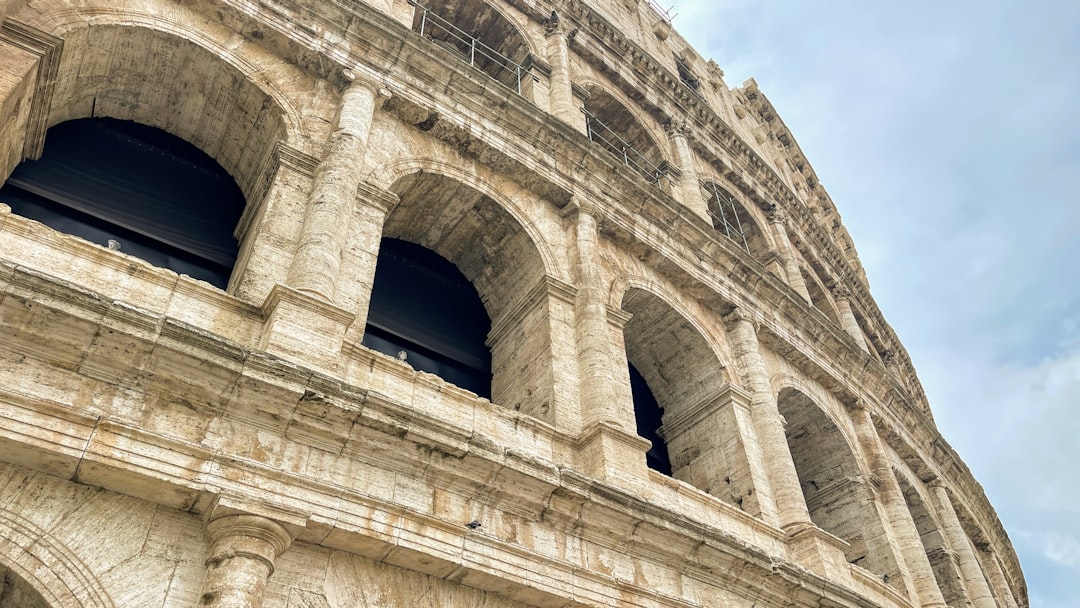 This image shows an upward view of the iconic Roman Colosseum, showcasing its grand arches and ancient travertine stone...