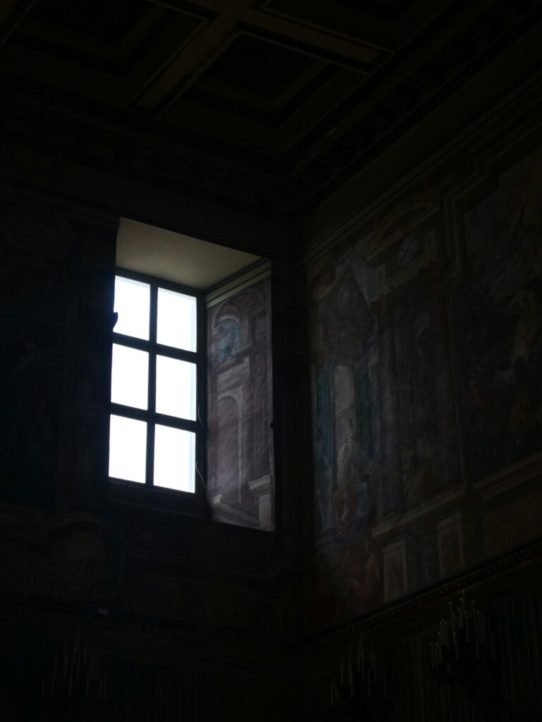 A dark room with a window and a painting on the wall