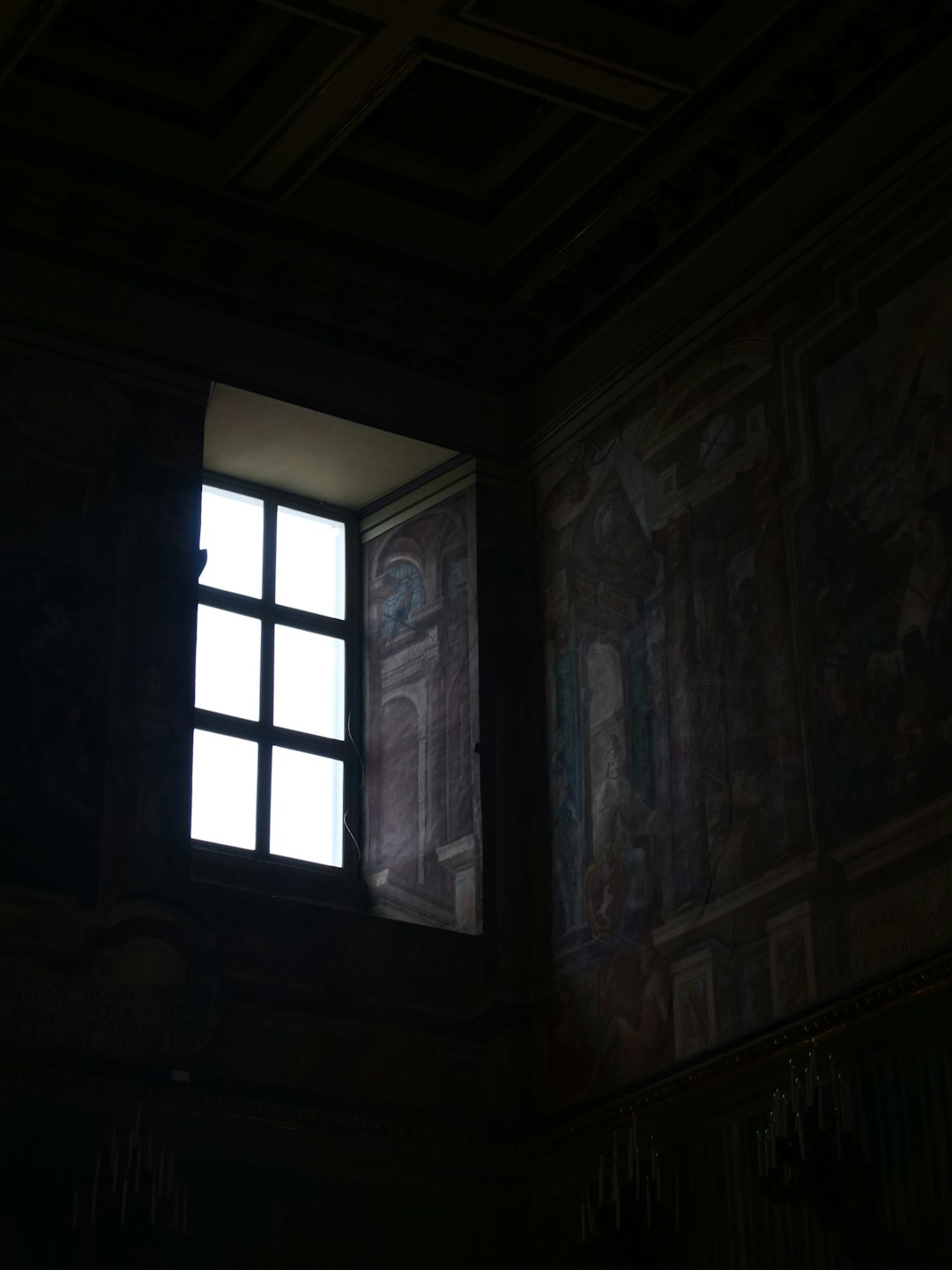 A dark room with a window and a painting on the wall
